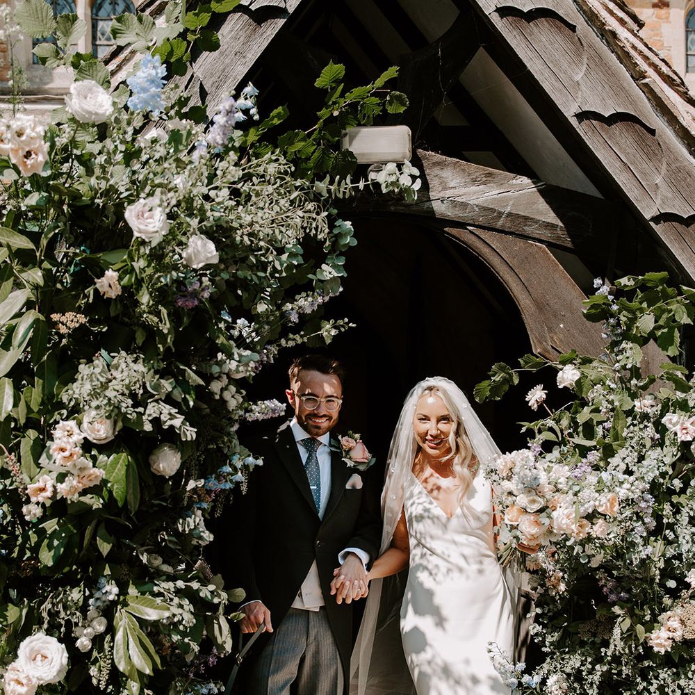 The bride and groom walk out of the church after their ceremony in between two flower columns 