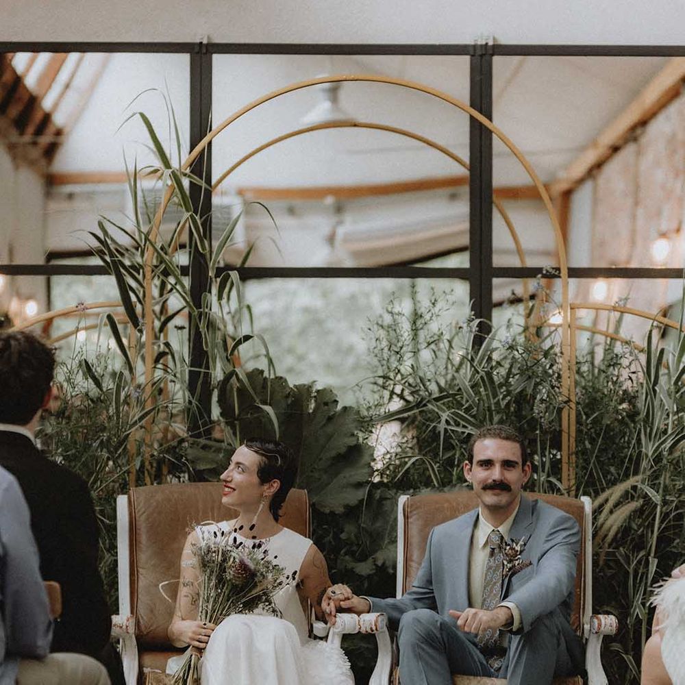 Lisa holds DIY bridal bouquet and sits beside Gabriel during non denominational wedding ceremony in France 