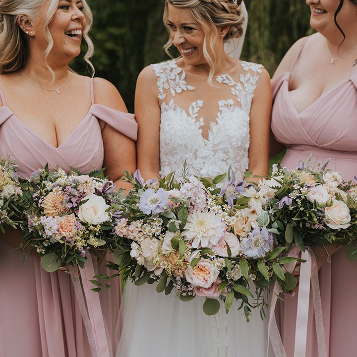Bridesmaids in pink off the shoulder bridesmaid dresses with the bride in lace wedding dress holding pastel wedding bouquet 
