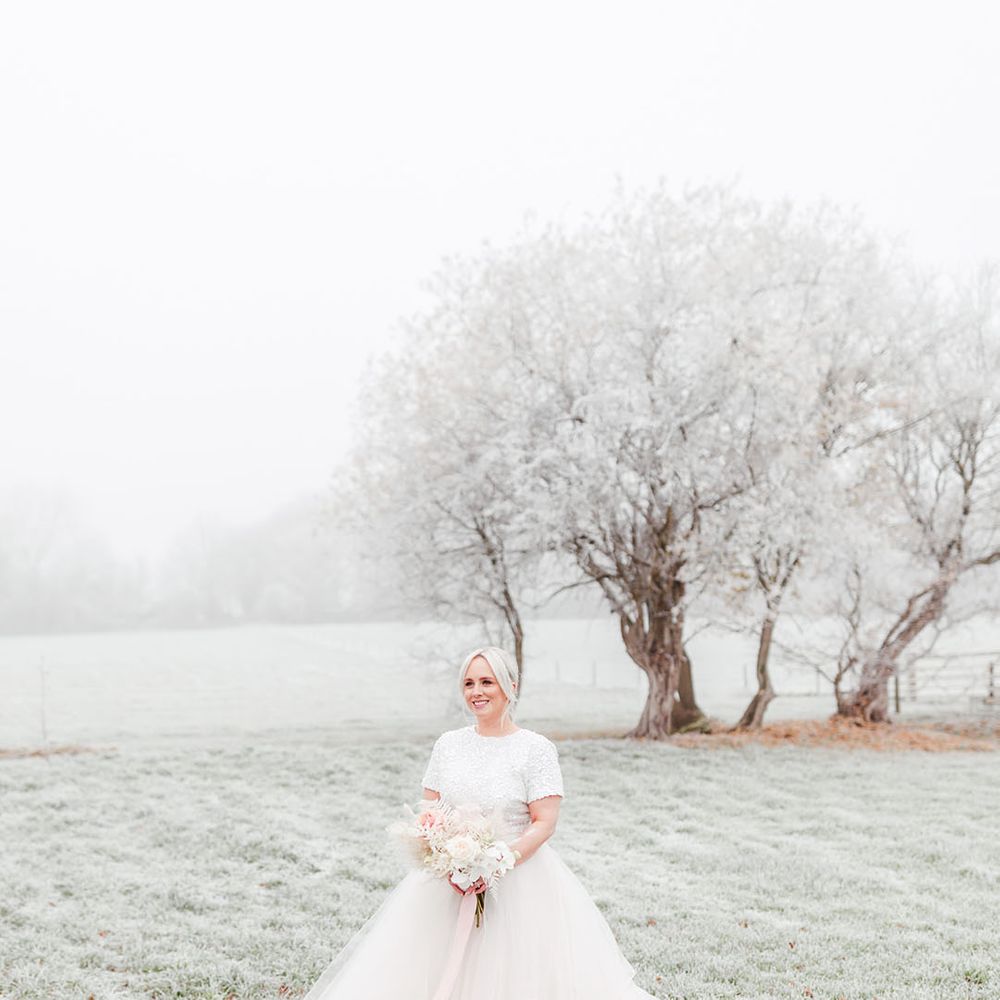 Bride in beaded sparkly top with a tulle bridal skirt holding a pink and white flower bouquet with pink ribbon for winter wedding 