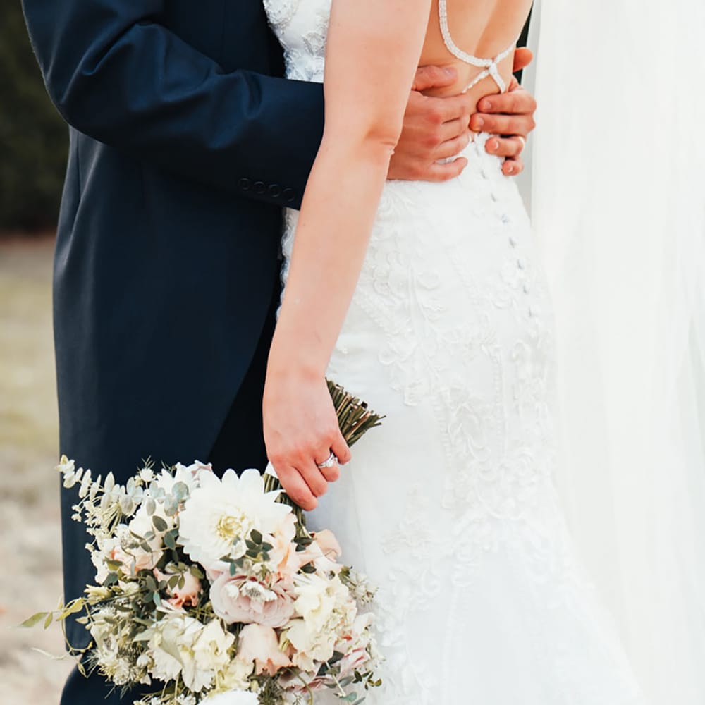 Bride in open back wedding dress with sparkly and button back detail being embraced by the groom 