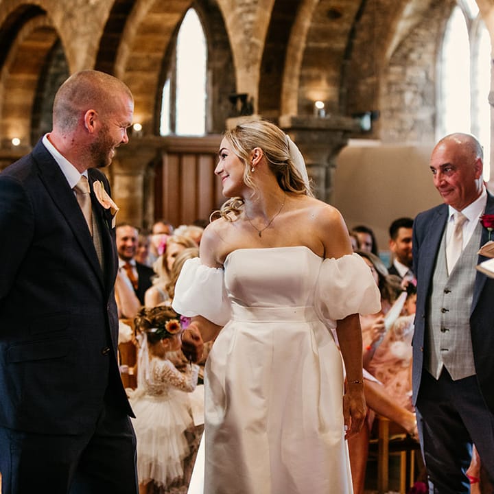 Father of the bride watches the bride greet the groom at the end of the aisle 