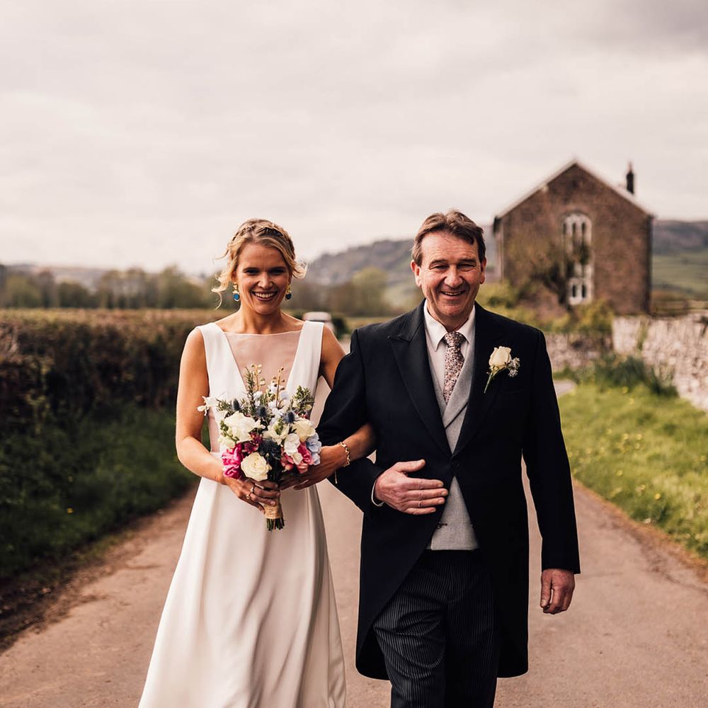 Father of the bride in a grey and black morning suit walking with the bride to the church 