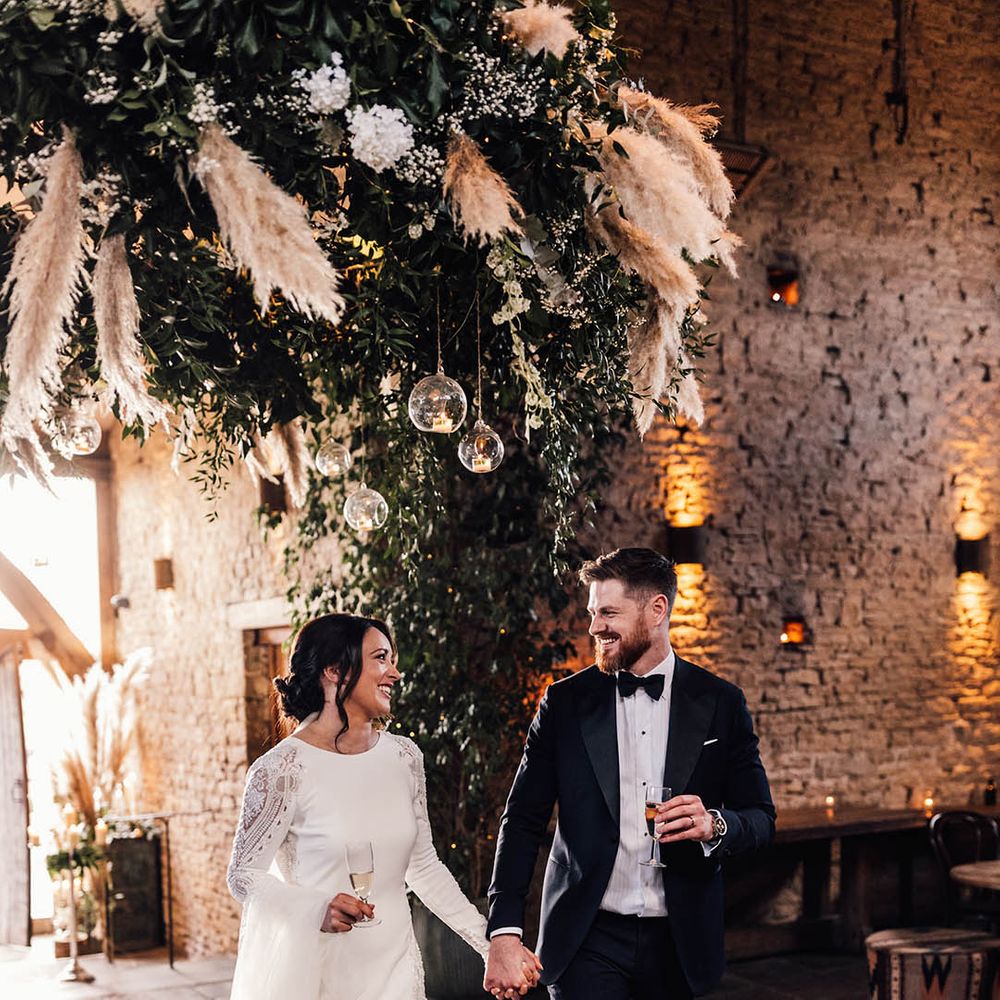 The bride and groom walk into the rustic barn wedding venue decorated with hanging floral installation 