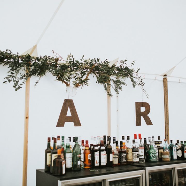 Marquee wedding reception with mini fridges and alcohol bottles with rustic wooden letter lights sign 