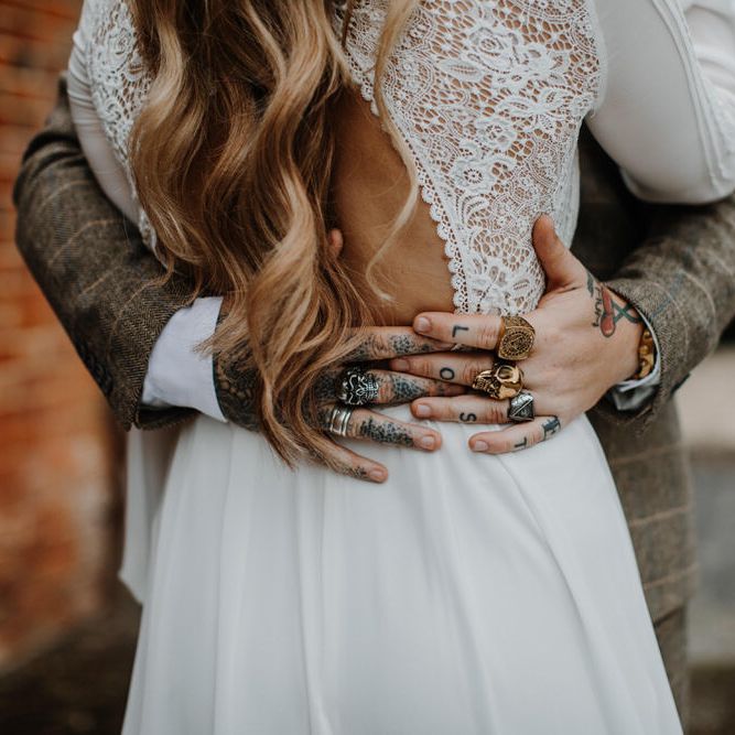 Groom hugging his wife with cutout back bridal dress with tattooed hands and skull rings 
