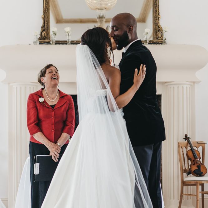 Bride in a strapless Oleg Cassini wedding dress and cathedral length veil kissing her groom at the altar 