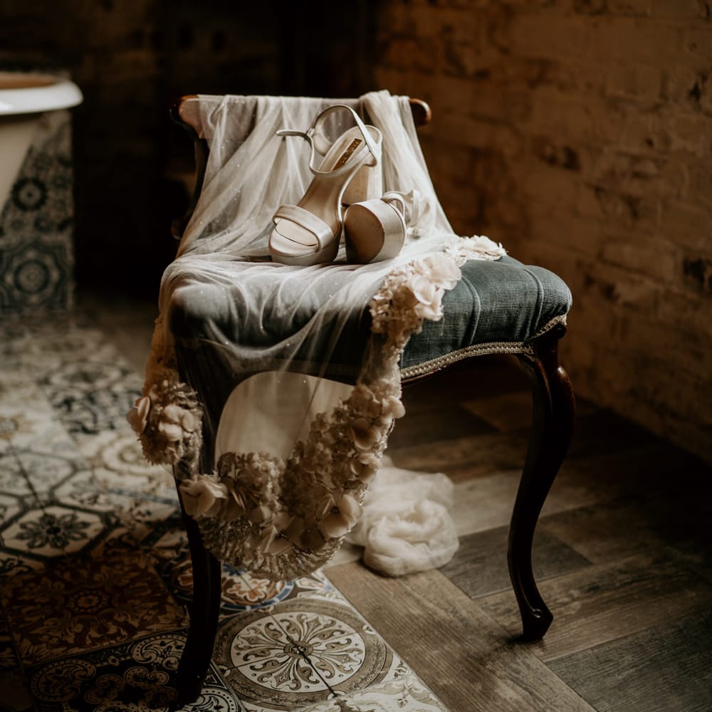 Beige wedding veil with flower applique detail and platform shoes draped over a velvet chair 