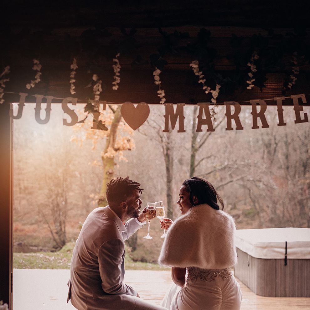 Bride & groom sit together underneath Just Married sign on decking 