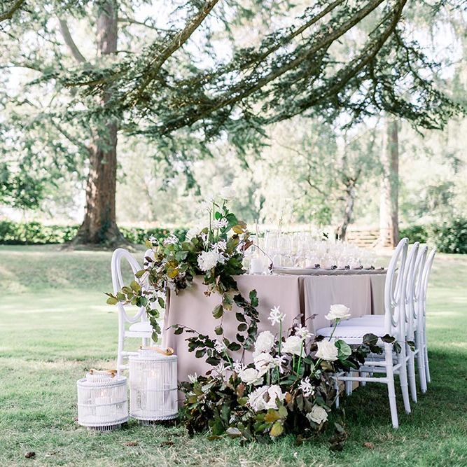 Intimate outdoor wedding reception table with linen tablecloth, white and green flower arrangements and white chairs 