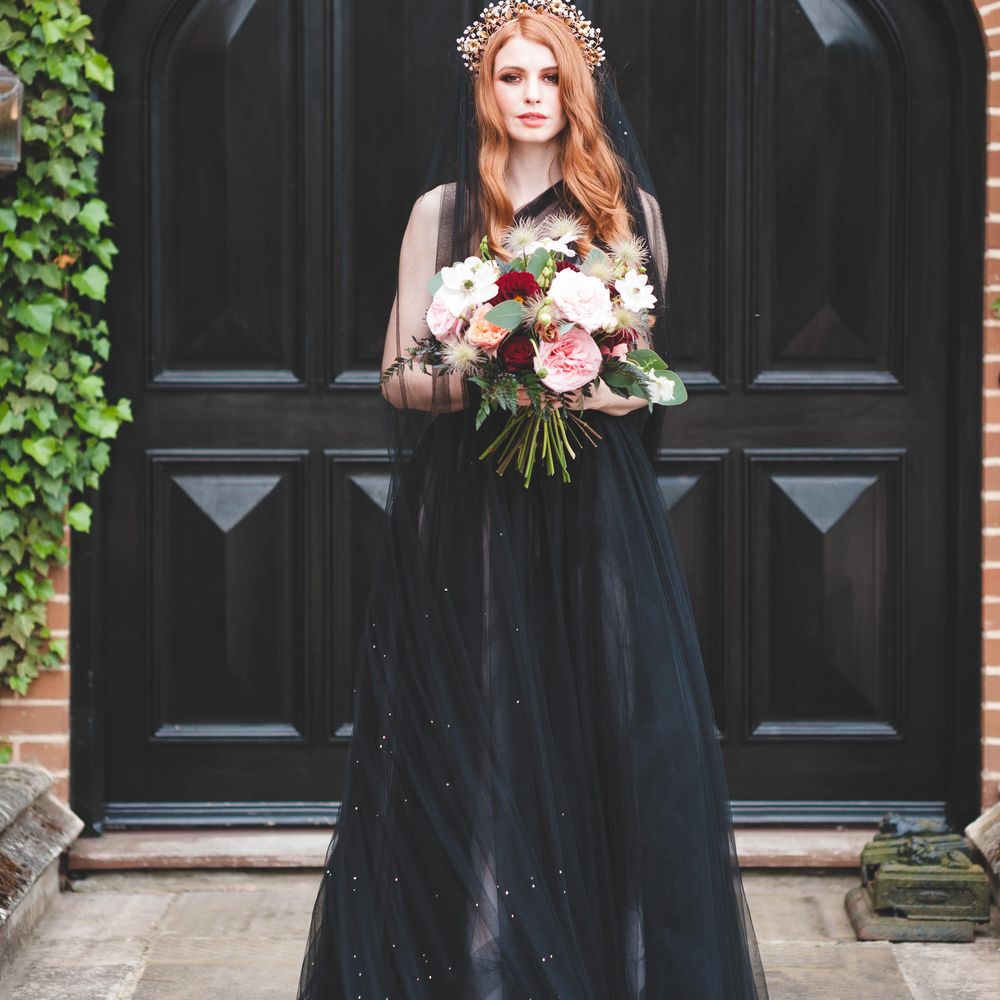 Bride with long auburn hair wearing a bridal crown holding a red, white and pink bouquet in a black tulle wedding dress 