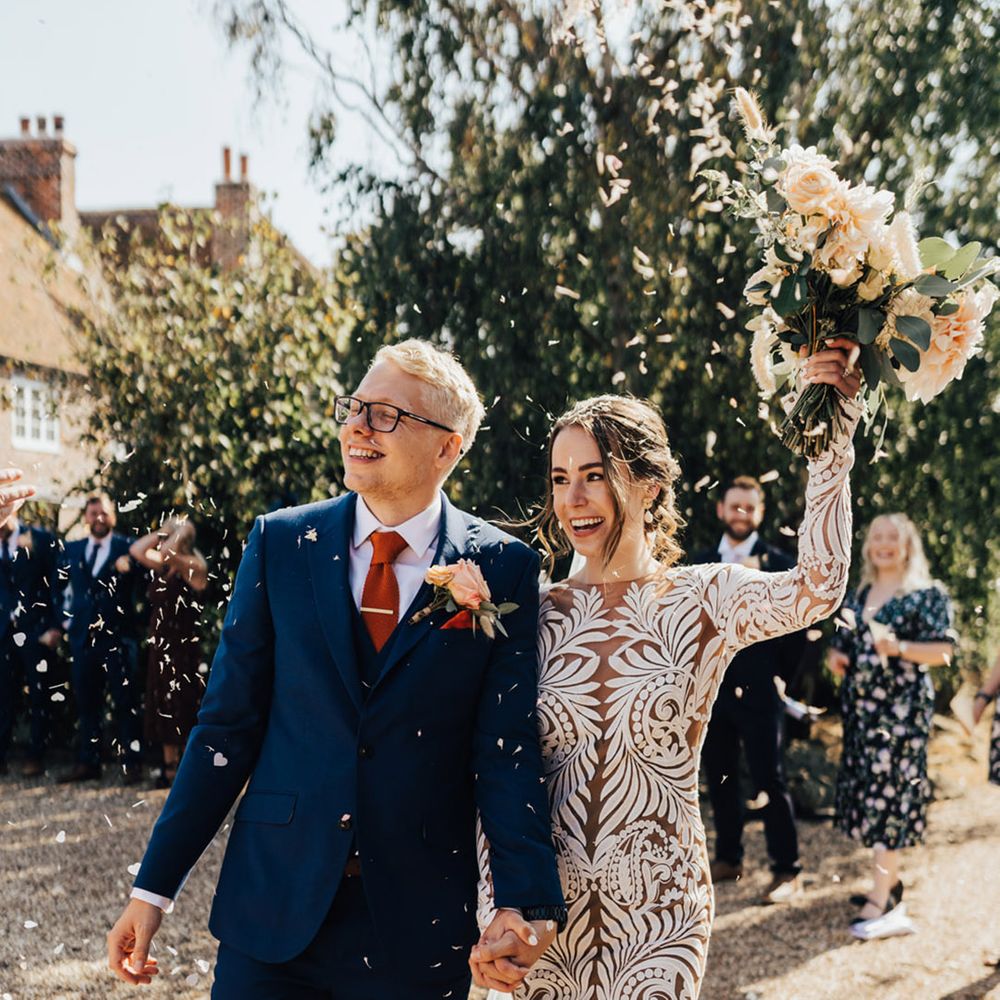Groom in navy fitted suit & waist jacket with orange silk tie with Bride in Boho Long detailed wedding dress with bunny tails & pale pink roses bouquet 