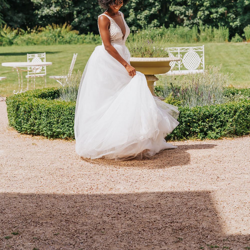 Black bride with short afro hair twirling her princess plunging neckline wedding dress with tulle skirt in the garden 