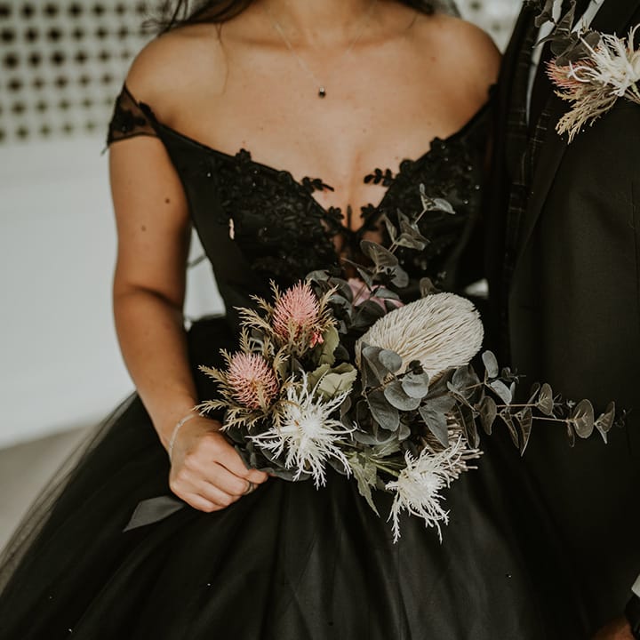 Bride wears homemade black wedding gown and holds floral bouquet 