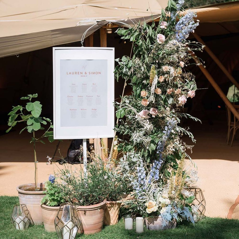 White and pink wedding seating/table chart with large pastel flower display and potted plants with candles in lanterns 