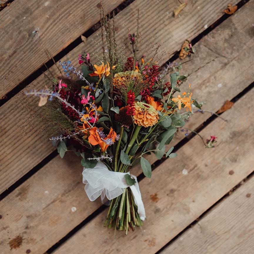 Yellow, red, orange, pink, purple, blue wedding bouquet tied with white sheer ribbon 