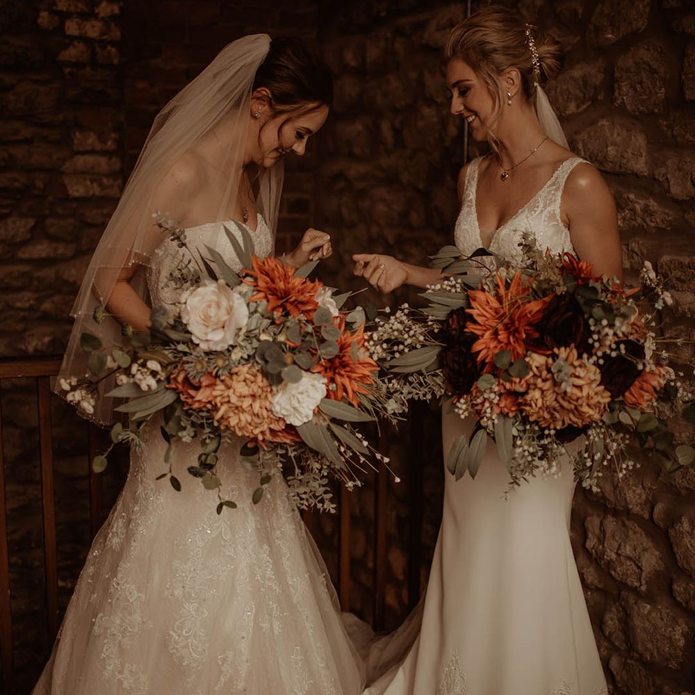 First look with two brides in fishtail wedding dresses holding oversized orange wedding bouquets 