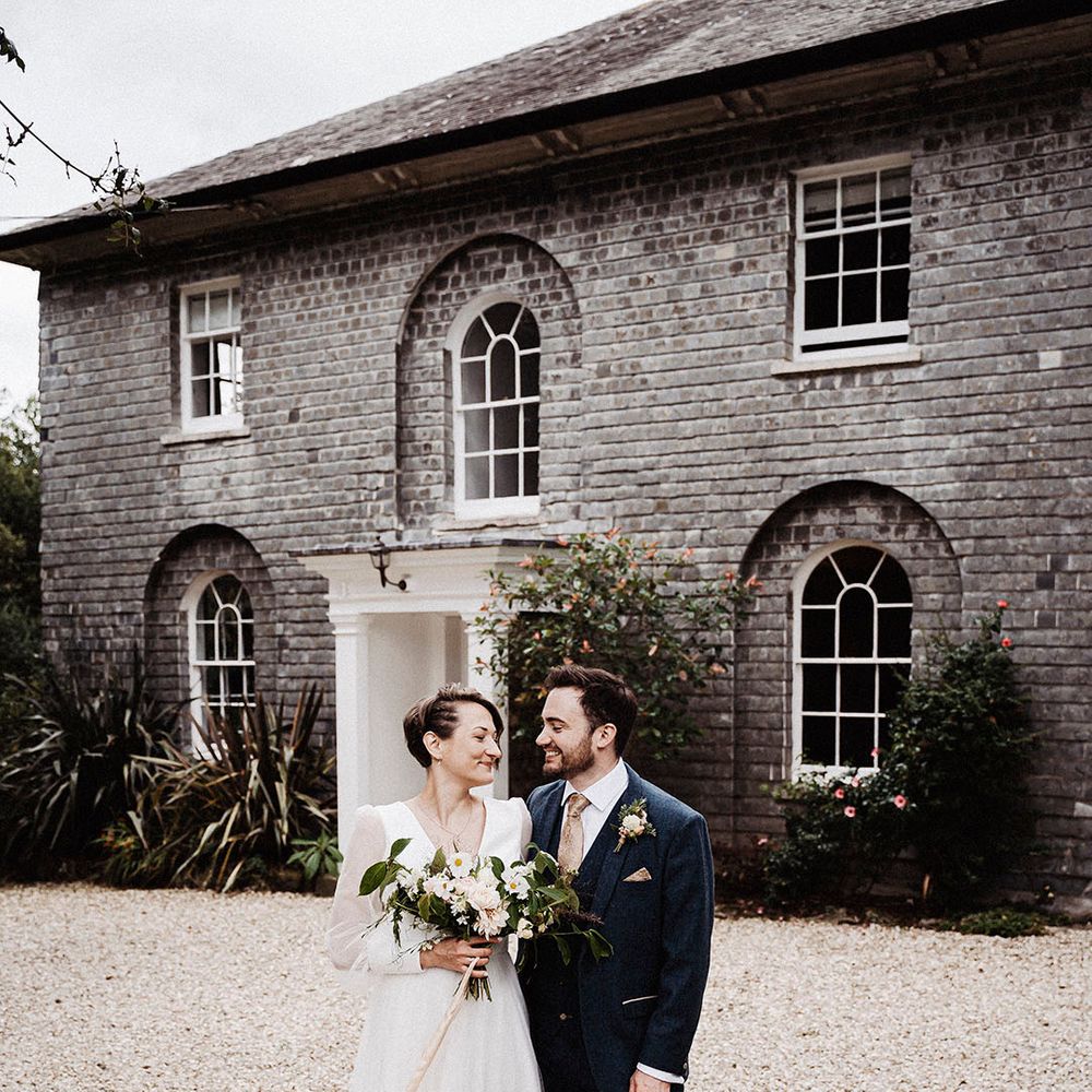 Bride in sheer long sleeve Sassi Holford wedding dress with groom in blue suit outside wedding venue, Treseren