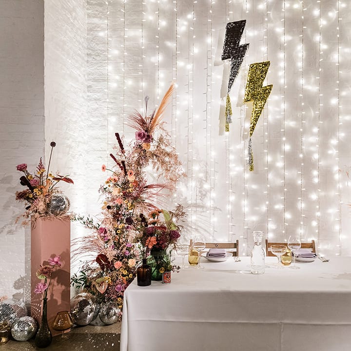 Sweetheart top table for bride and groom with fairy light backdrop with lightning decor and colourful flowers as well as disco balls