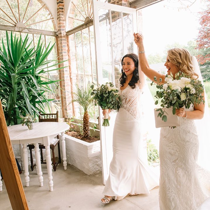 Brides walk into their wedding reception together holding hands 