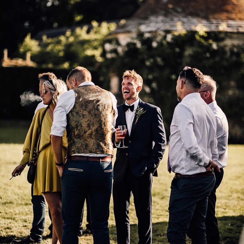 Groom laughs and socialises with the wedding guests for his outdoor wedding 