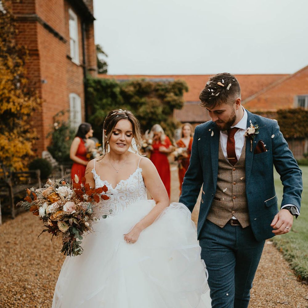 Bride carrying autumnal bouquet in a Blush by Hayley Paige wedding dress with groom in blue suit and burnt orange tie 