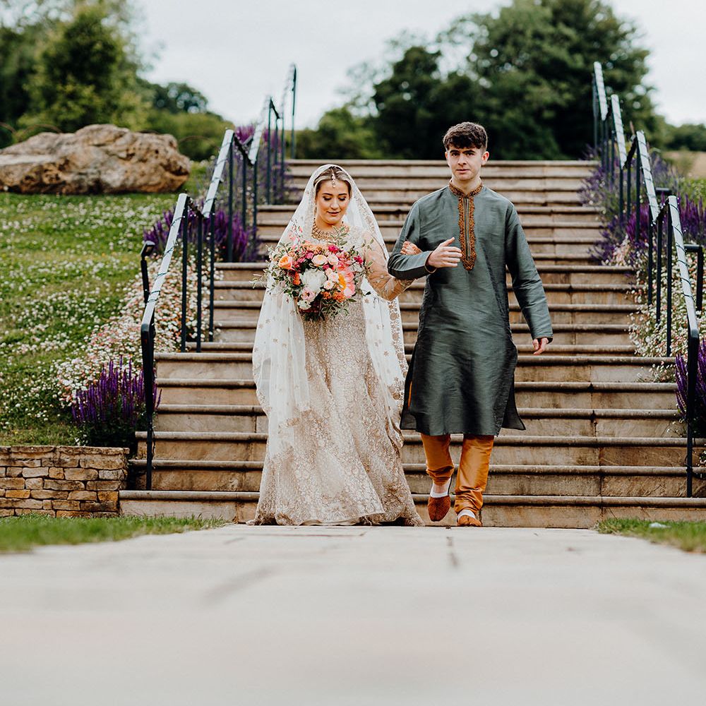 Bride wears traditional saree in white with embellishment walks down staircase with family member 
