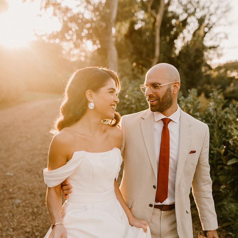 Bride in a structured off the shoulder wedding gown with the groom in a pale wedding suit and red tie for autumnal wedding at Chapel House Estate