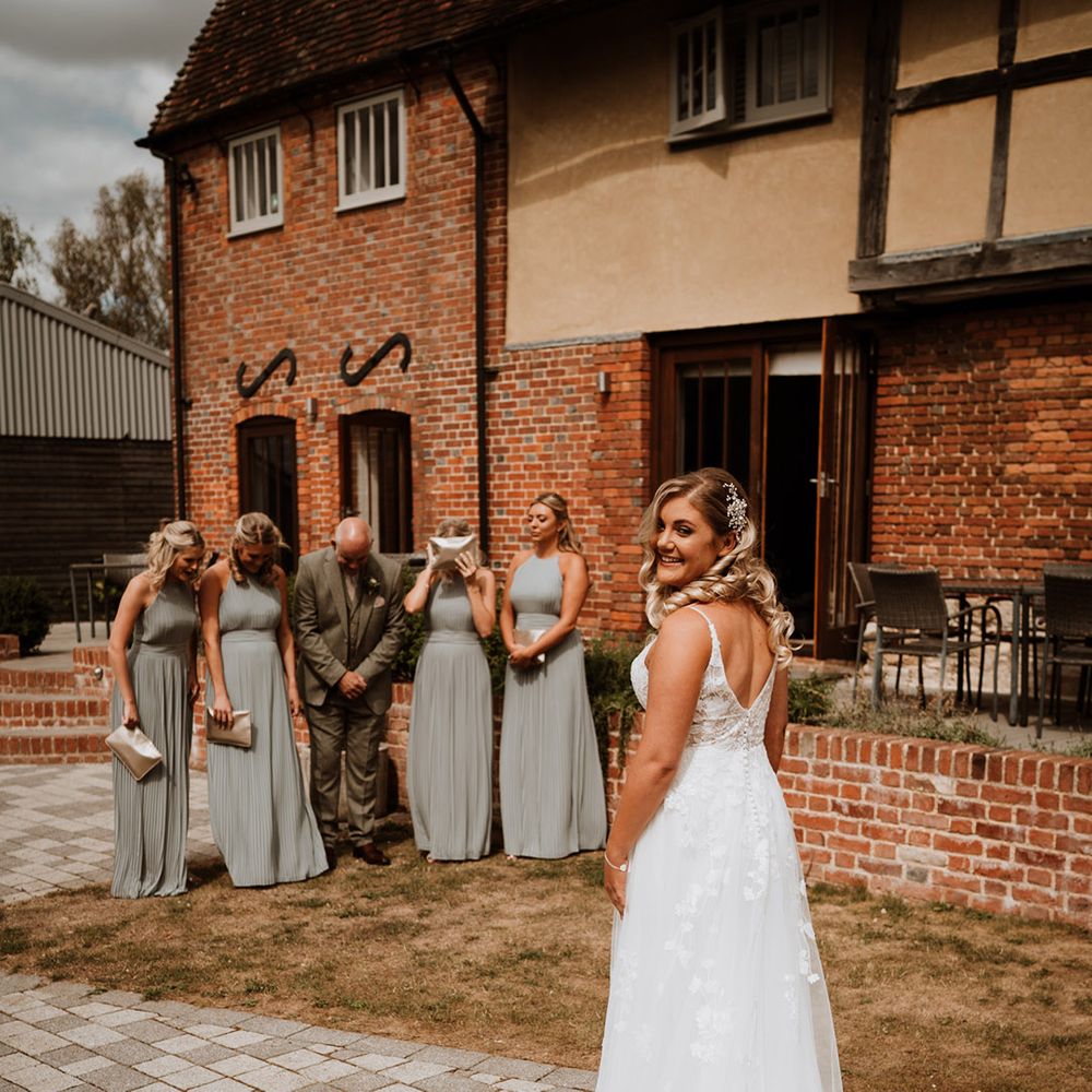 Each bridesmaid wears a sage pleated bridesmaid dress standing with the father of the bride as they hide their eyes before the first look 