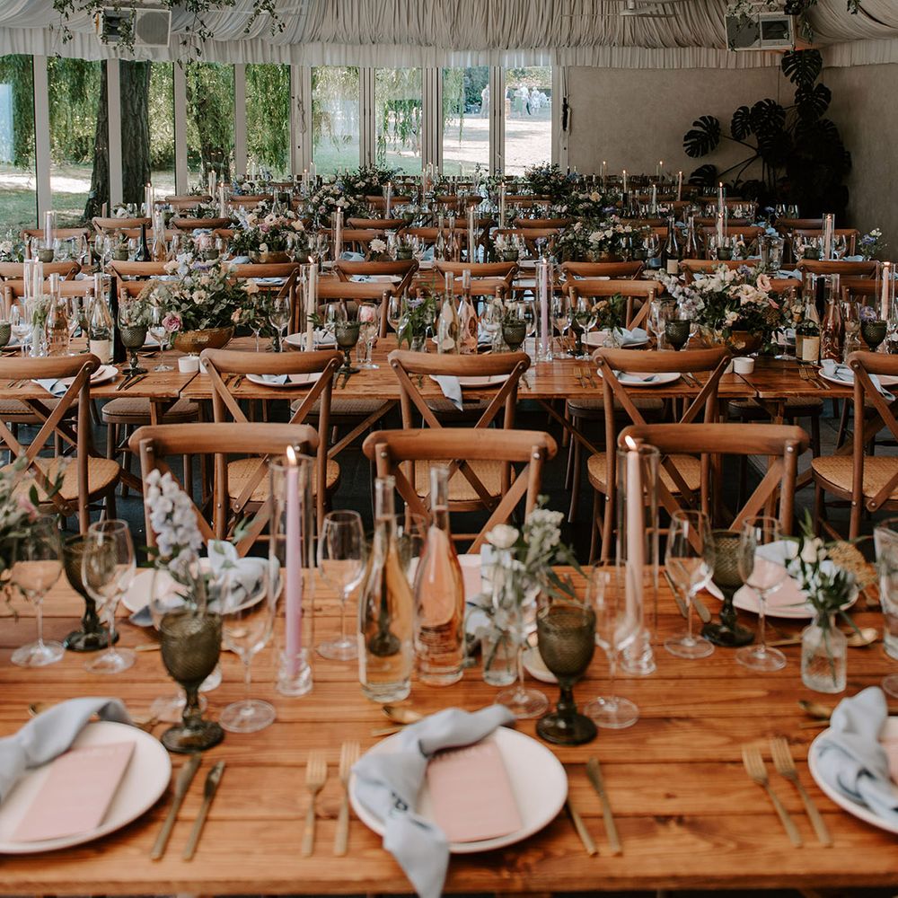 Marquee wedding reception with disco balls with decorative greenery and a pastel theme wedding table setting with blue napkins and pink menus 