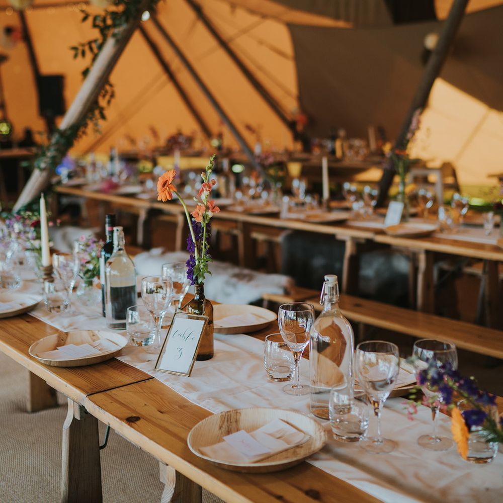 Rustic wooden banquet tables with white table runner and small colourful floral arrangements in tent 