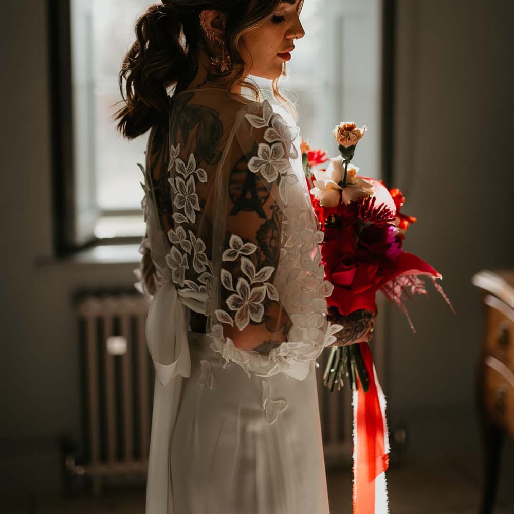 Bride in two piece bridal separates with puff sleeve sheer crop top with 3d appliqué flowers and full bodied silk skirt and gold bridal flower crown holding magenta and hot pink floral bouquet