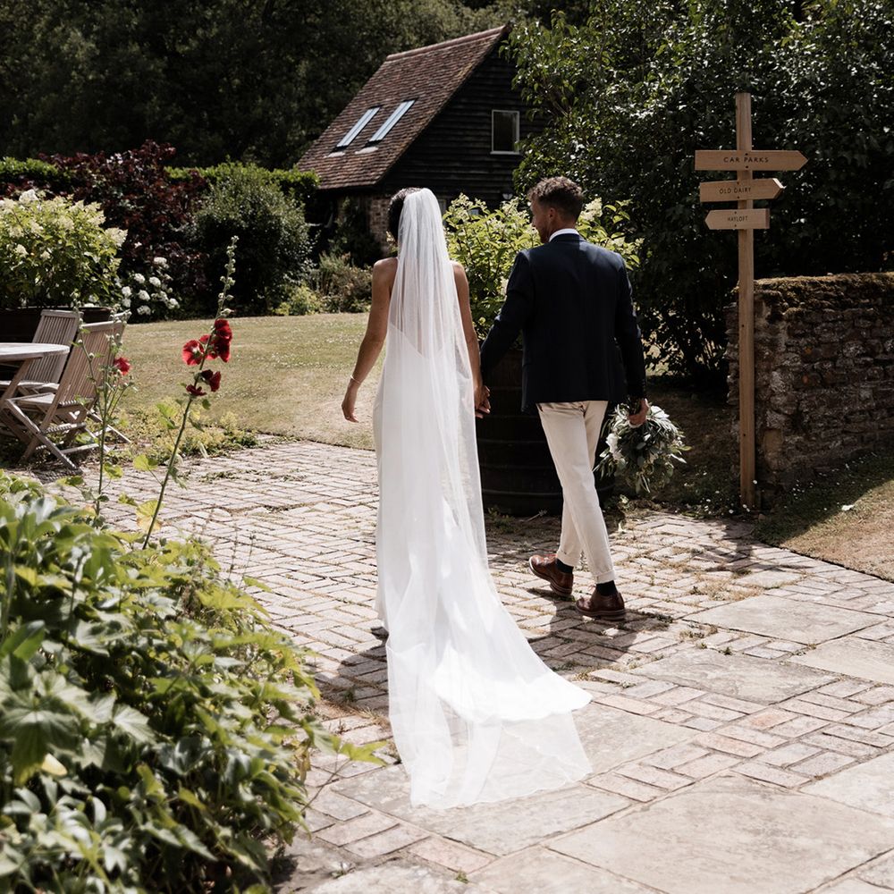 Bride in floor length veil walks alongside her groom at the Gate Street Barn rustic wedding venue 