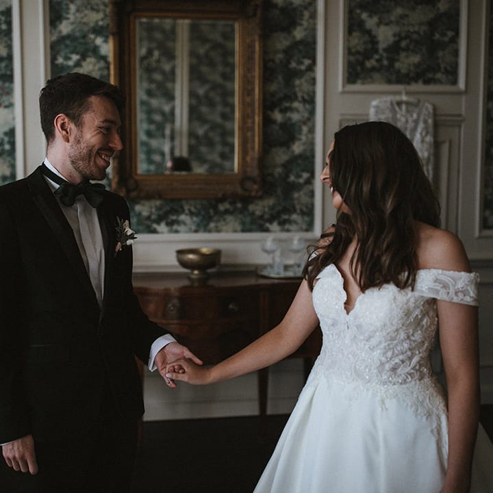 Man of honour in traditional black tie greets her and sees her in her wedding dress with the bride in a Pronovias wedding dress 