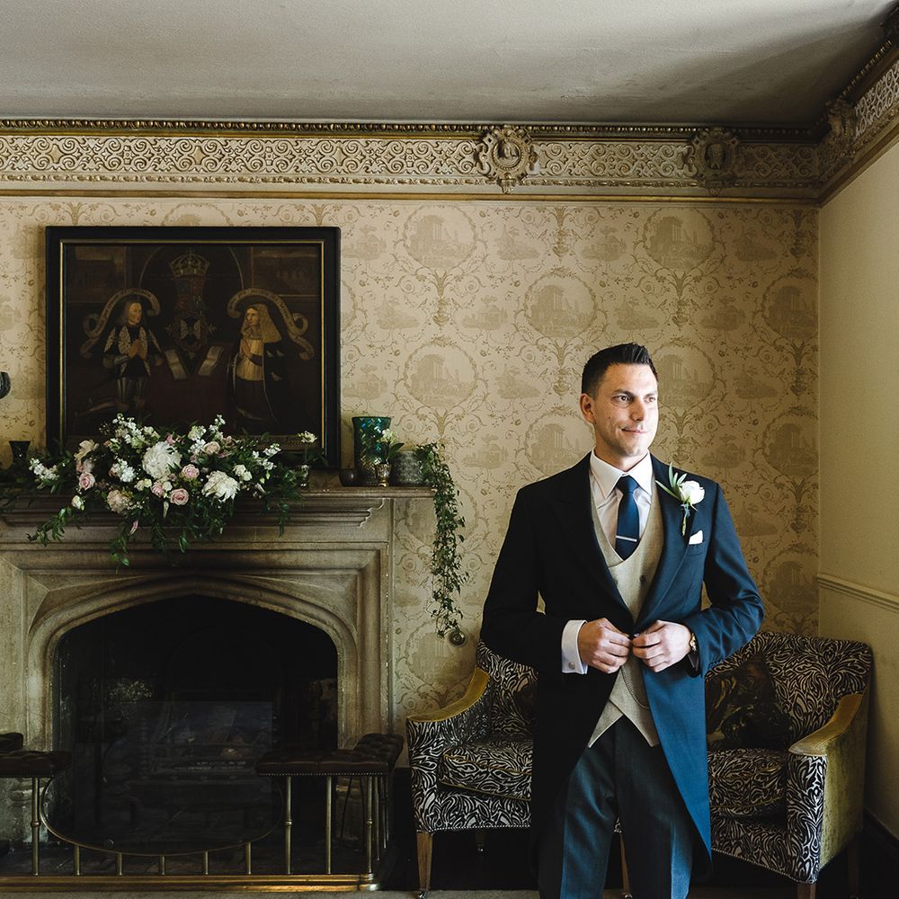 Groom in black morning suit with beige waistcoat and navy tie with silver tie clip for the wedding day 