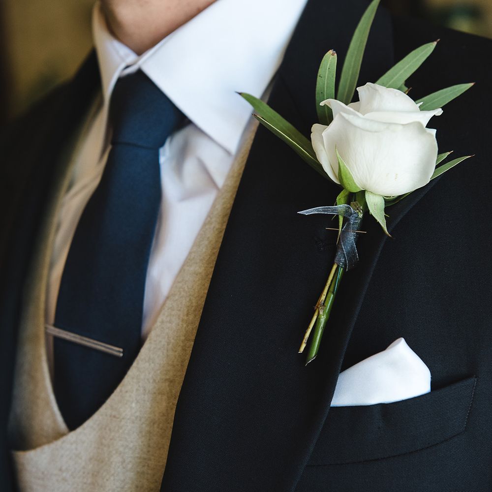Simple white rose buttonhole worn by the groom in a morning suit for the traditional wedding 