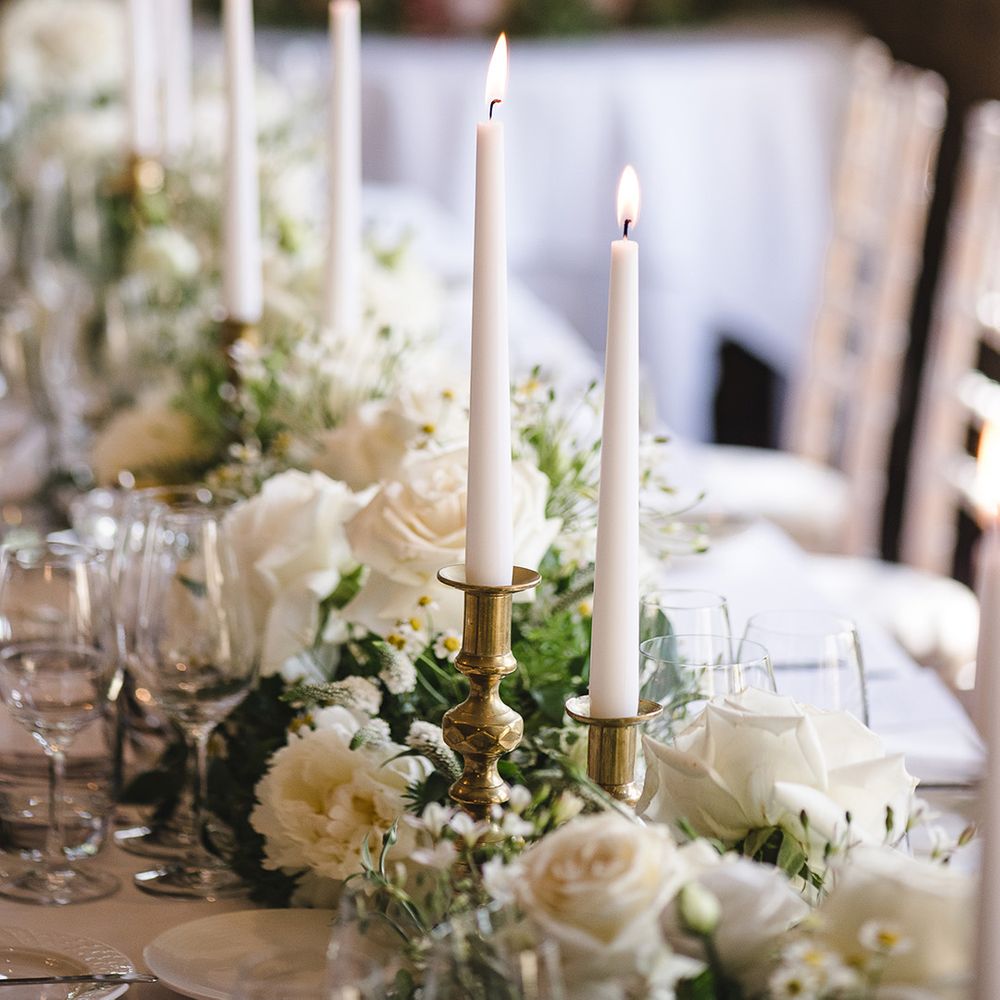 White taper candles in gold candle holders on the wedding table with white wedding flower table decorations 