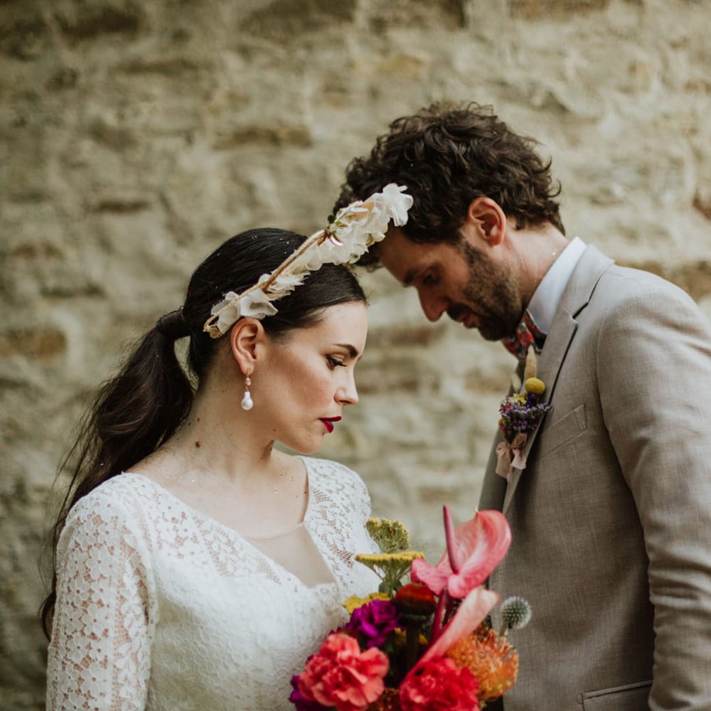 Bride in white floral bridal crown and red lip bridal makeup, holding pink bridal bouquet with groom in greige suit at outdoor wedding in Italy