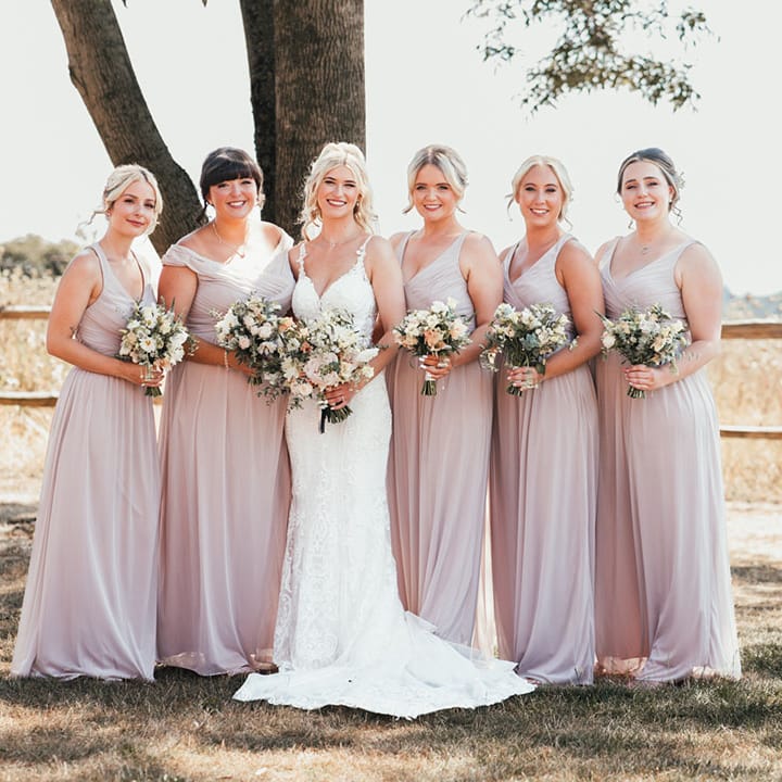 Pink bridesmaid dresses posing with the bride in a fitted lace wedding dress holding white wedding bouquets 