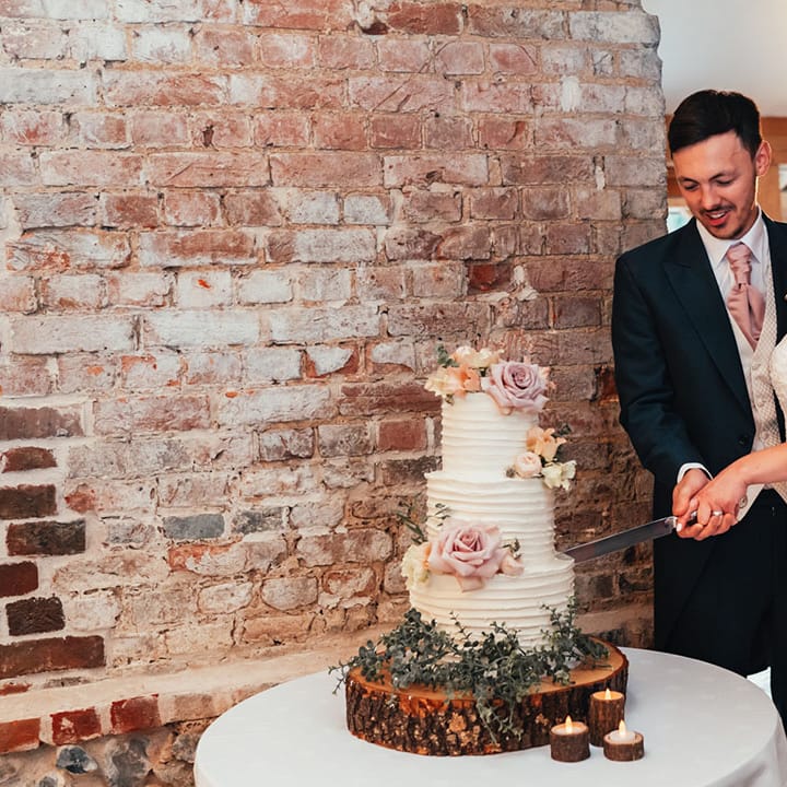 The bride and groom cut their three tier white iced wedding cake together with rose cake decorations 