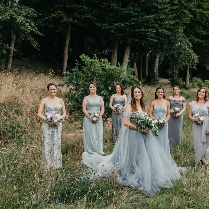 Bride in ethereal tulle blue wedding dress standing in a field with bridal party wearing mismatched blue bridesmaid dresses 