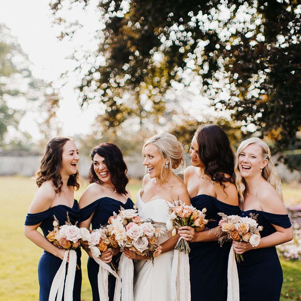 Bride in off the shoulder wedding dress standing with bridesmaids in off the shoulder navy bridesmaid dresses 