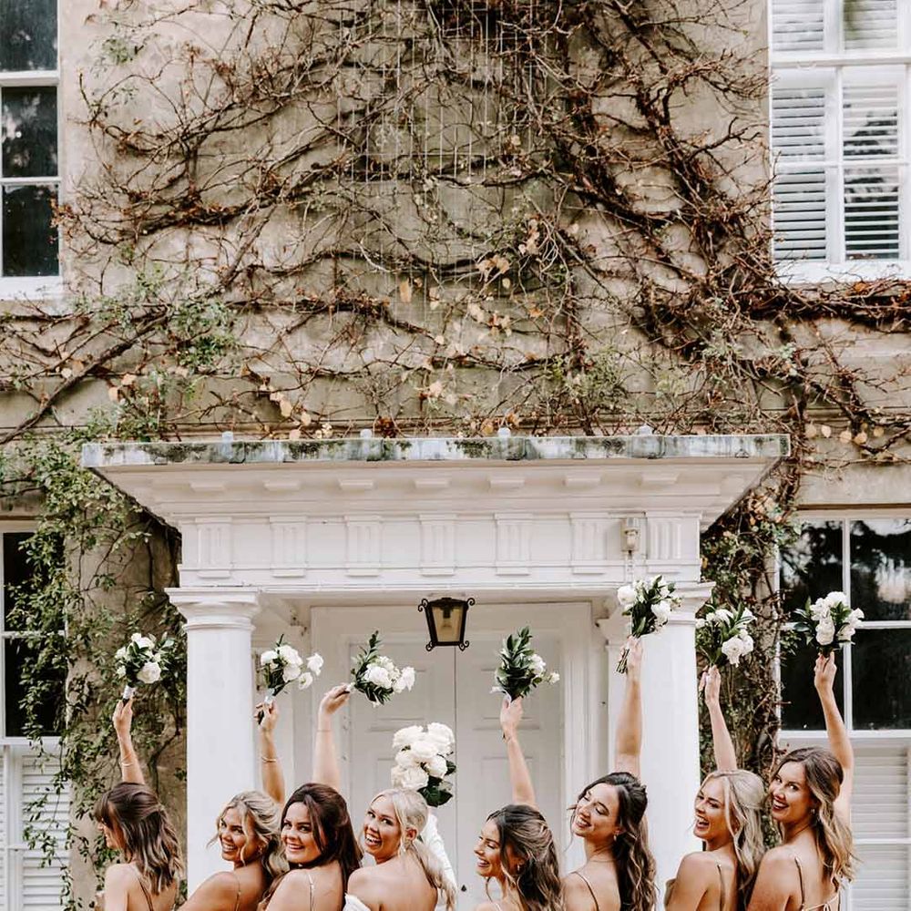 Bride in off the shoulder bodycon wedding dress standing with bridal party in sleeveless satin champagne gold bridesmaid dresses 