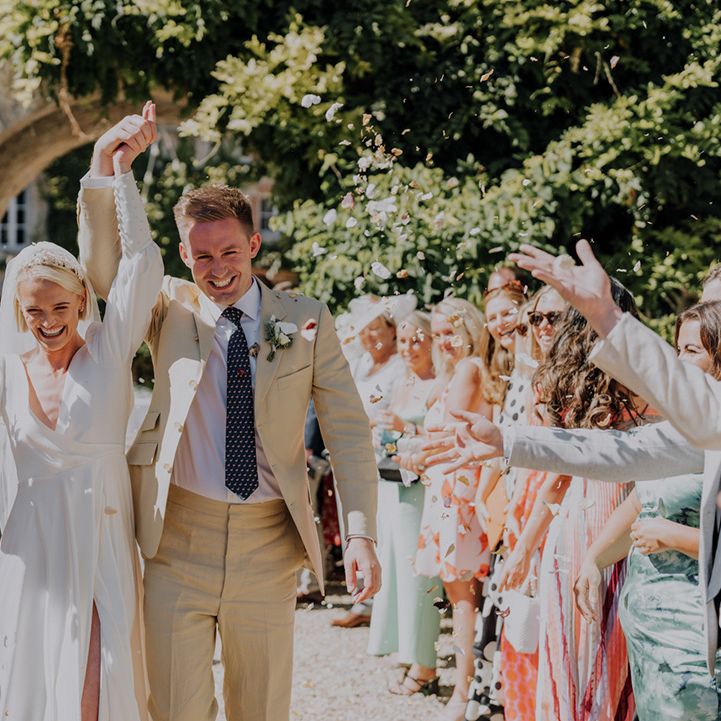 Confetti moment with bride in a long sleeve Emma Beaumont wedding dress and groom in a beige suit 