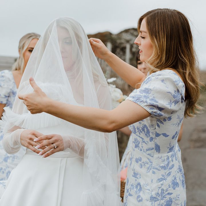 The bridesmaids in blue patterned bridesmaid dresses help the bride with her veil