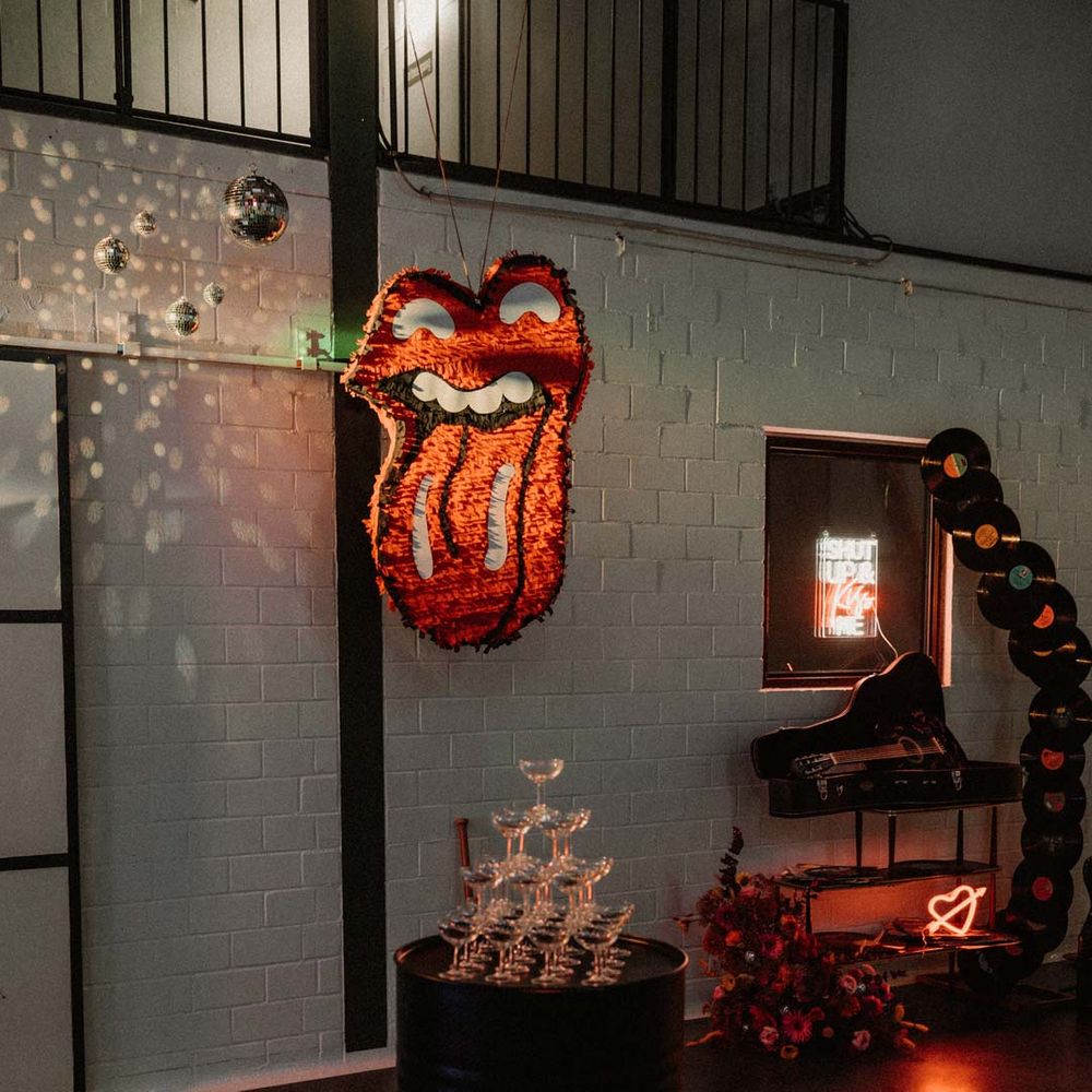 Wedding champagne tower with contemporary wedding neon sign in shape of fire emoji and Rolling Stones rock and roll wedding piñata 
