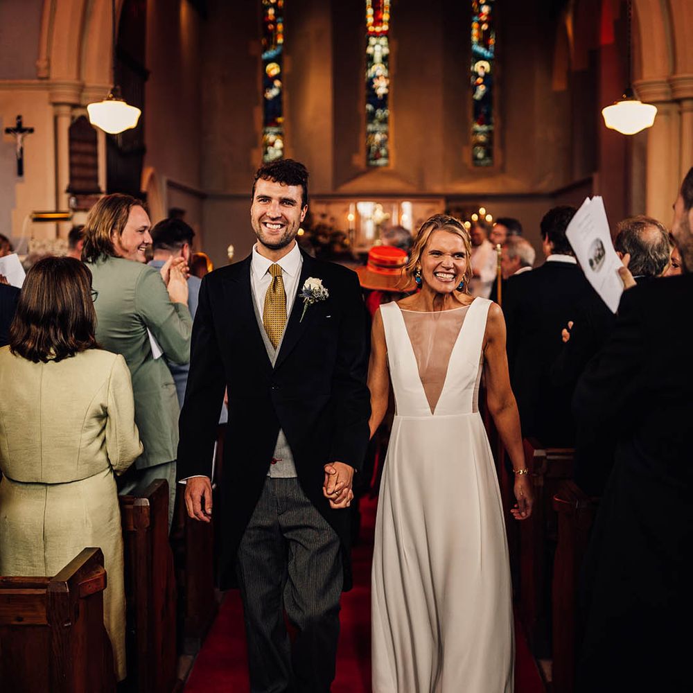 Groom in traditional wedding morning suit with yellow tie walking hand in hand with bride in Andrea Hawke wedding dress 