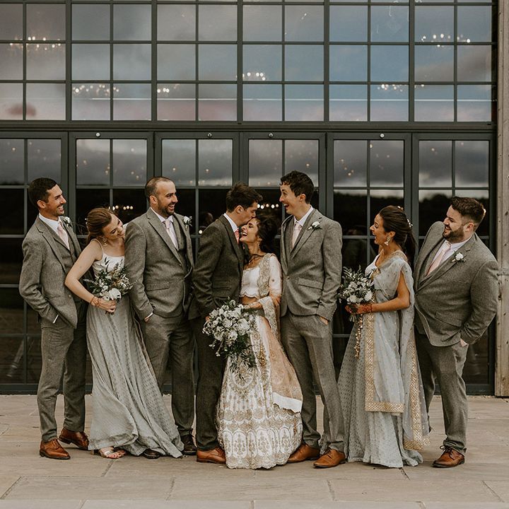 Group wedding photo of the whole wedding party with the bridesmaids and groomsmen in grey wedding outfits and bride and groom 