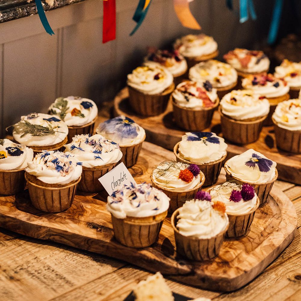 Wedding dessert table with cupcakes of different flavours decorated with edible flowers with rainbow wedding theme decorations and ribbons