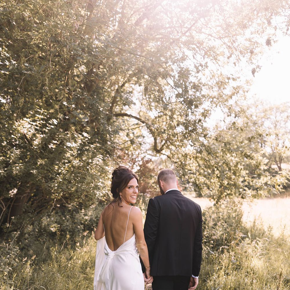 Bride in low back satin slip wedding dress walking with the groom during golden hour 